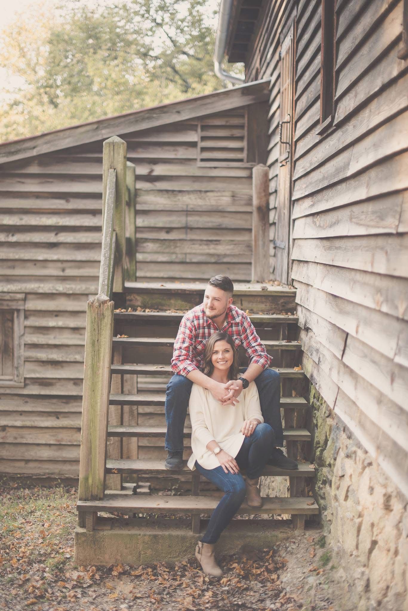 Couple posing on rustic wooden steps of a log cabin during a fall engagement photo session.