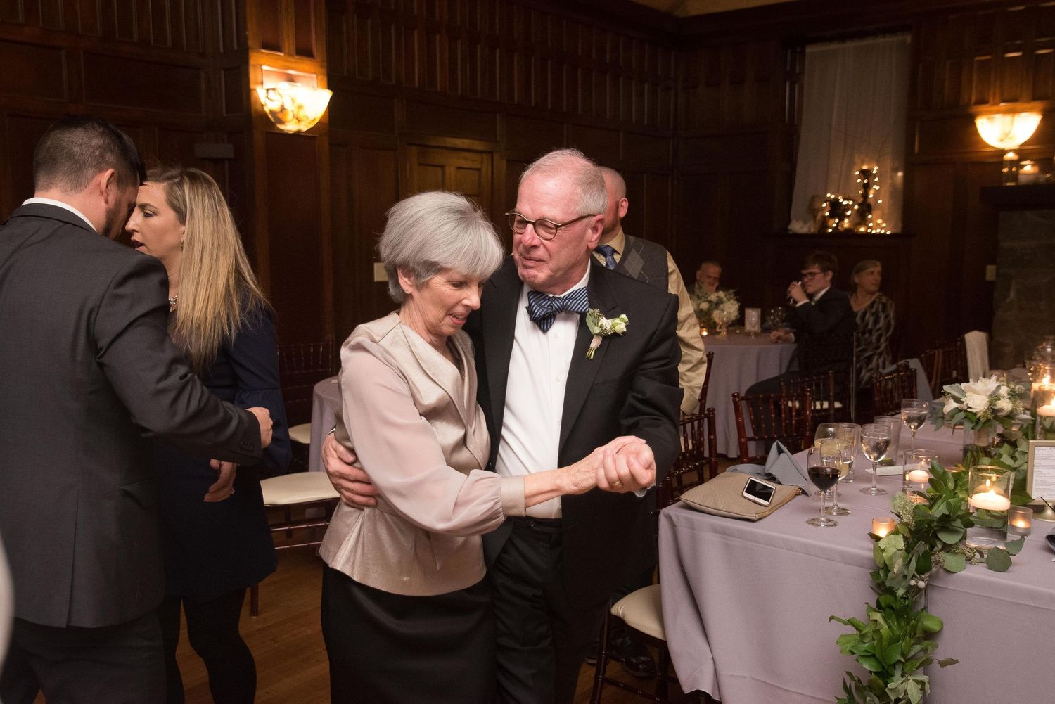 Elderly couple dancing elegantly at a wedding reception in a wood-paneled ballroom.