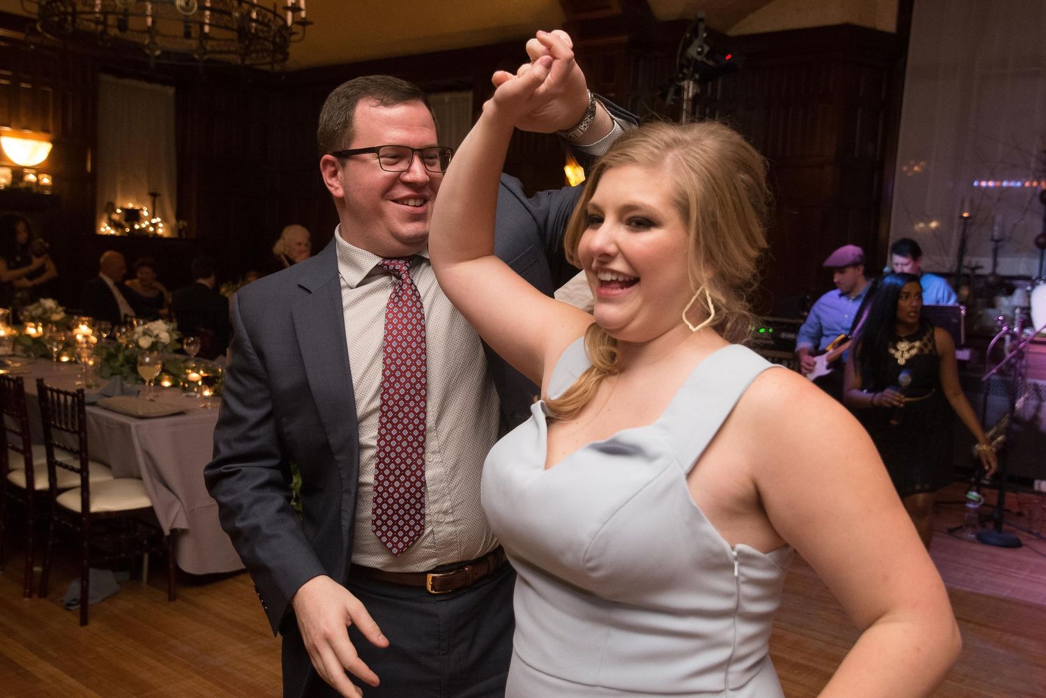 Couple dancing joyfully at a wedding reception in an elegant venue, man in suit and woman in silver dress.