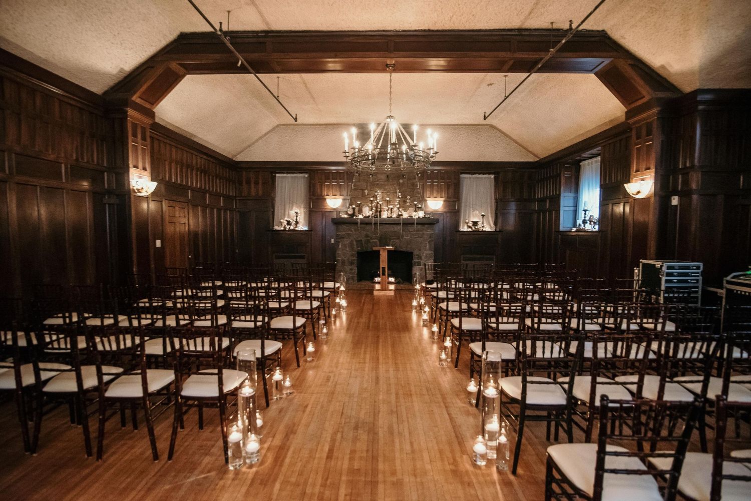 Elegant wood-paneled wedding ceremony venue with chandelier, chiavari chairs, and candlelit aisle on hardwood floors.