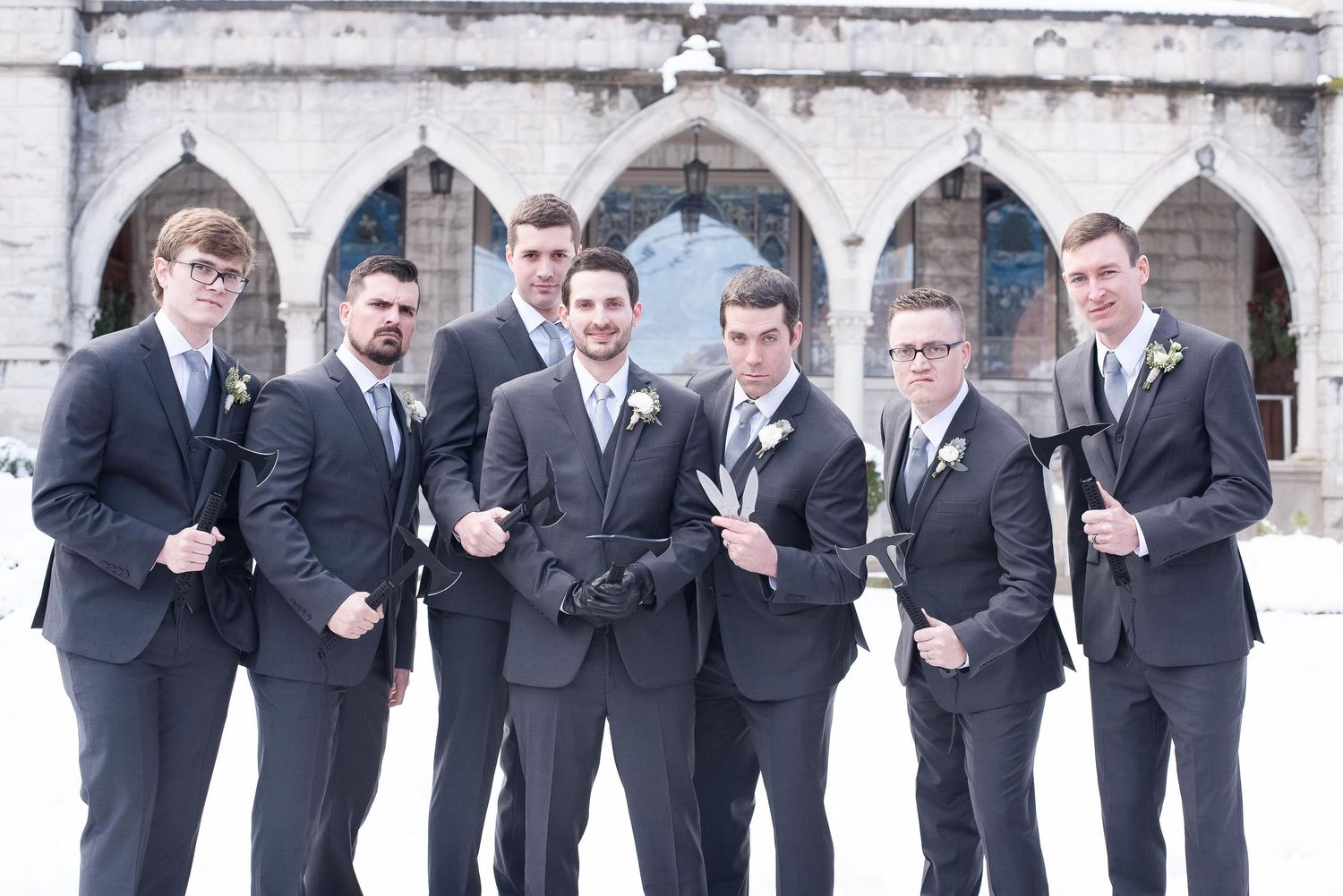 Groom and groomsmen in dark suits with boutonnieres posing outside a stone church in winter.