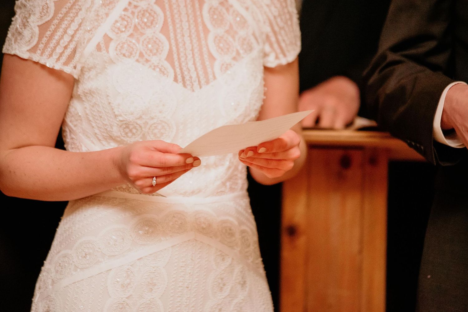 Bride in lace wedding dress reading vows from paper at altar during wedding ceremony.