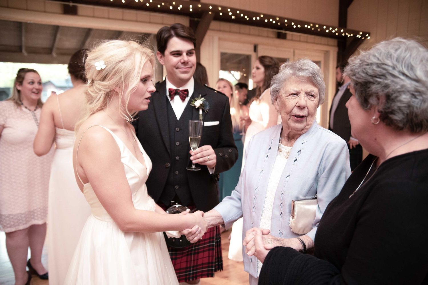 Bride and groom in Scottish kilt greeting elderly guests at wedding reception venue.
