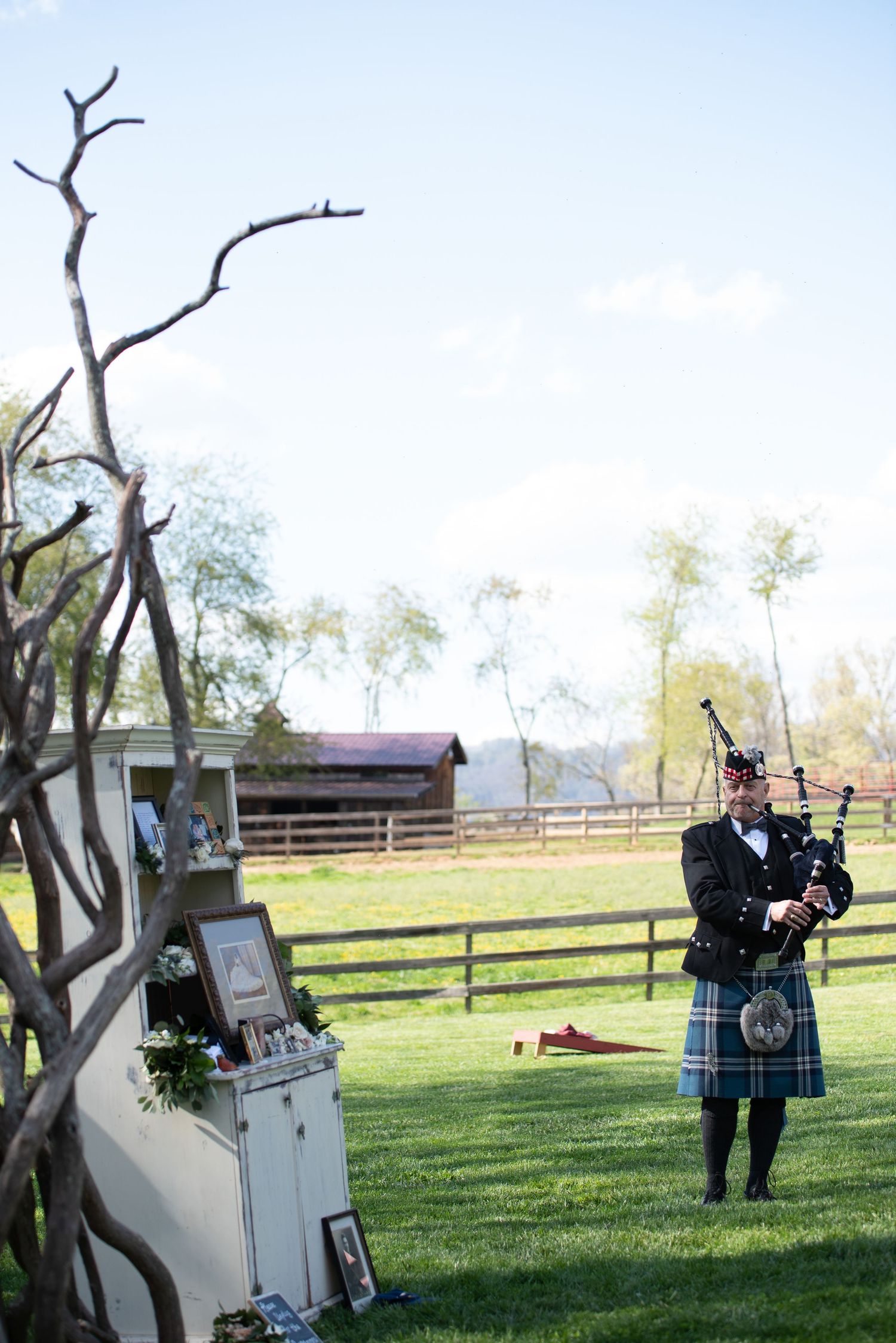 Bagpiper in traditional Scottish kilt performing at outdoor wedding venue on a sunny day.