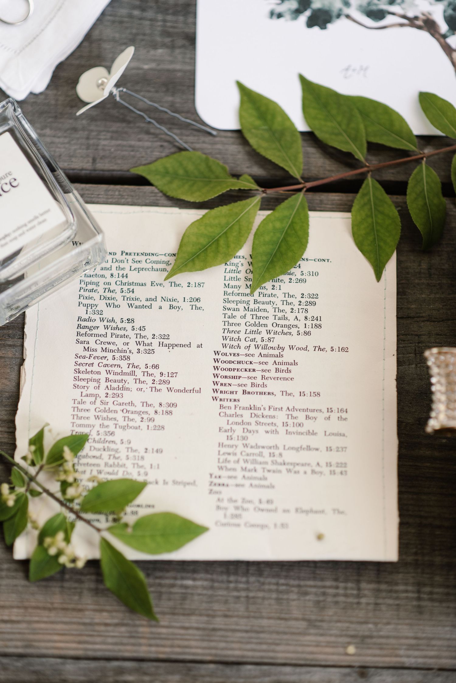 Vintage book table number with green leaves used as elegant wedding reception decor on rustic wood table.