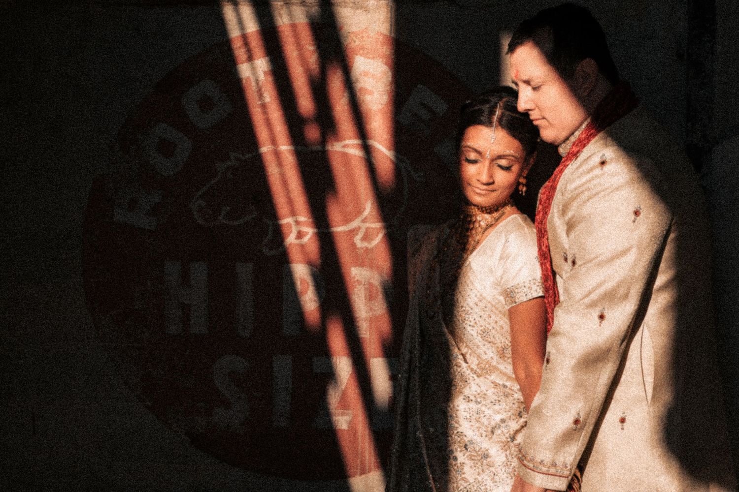 Couple in traditional Indian wedding attire sharing an intimate moment in dramatic light and shadow.