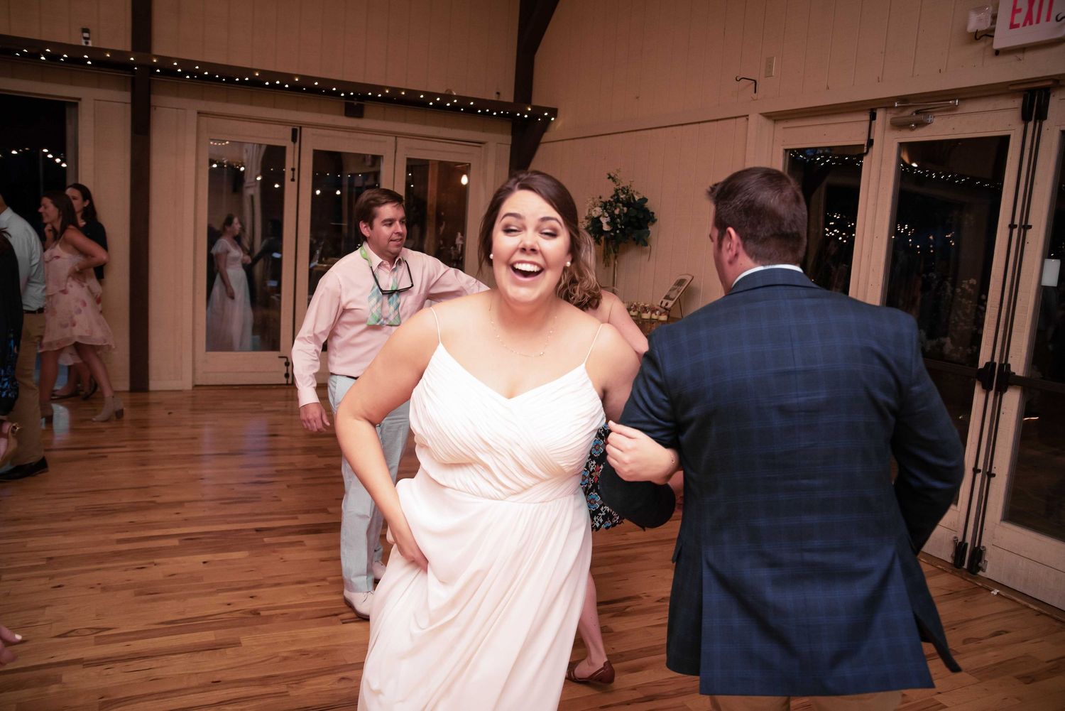 Bride in white dress laughing joyfully while dancing with groom in blue suit at elegant wedding reception.