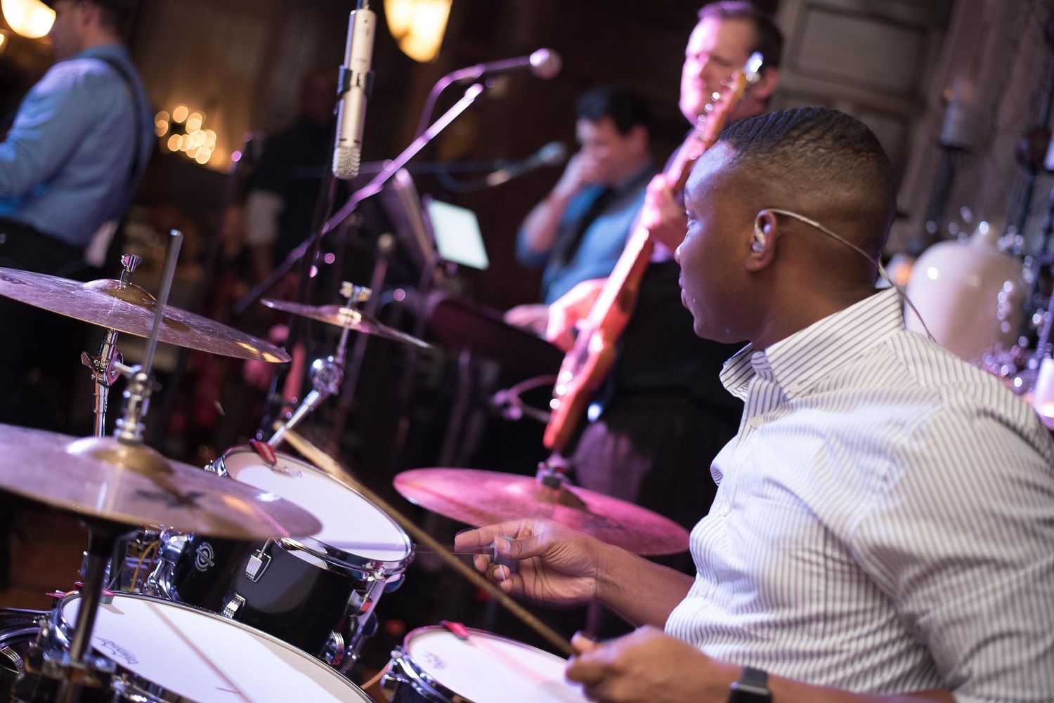 A musician plays drums at a live jazz band performance in a dimly lit venue.