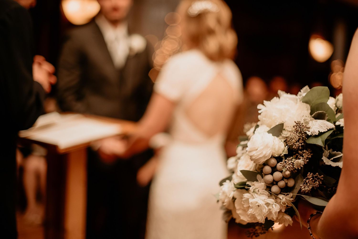 Bride and groom exchanging vows at wedding ceremony with elegant white floral bouquet in foreground.