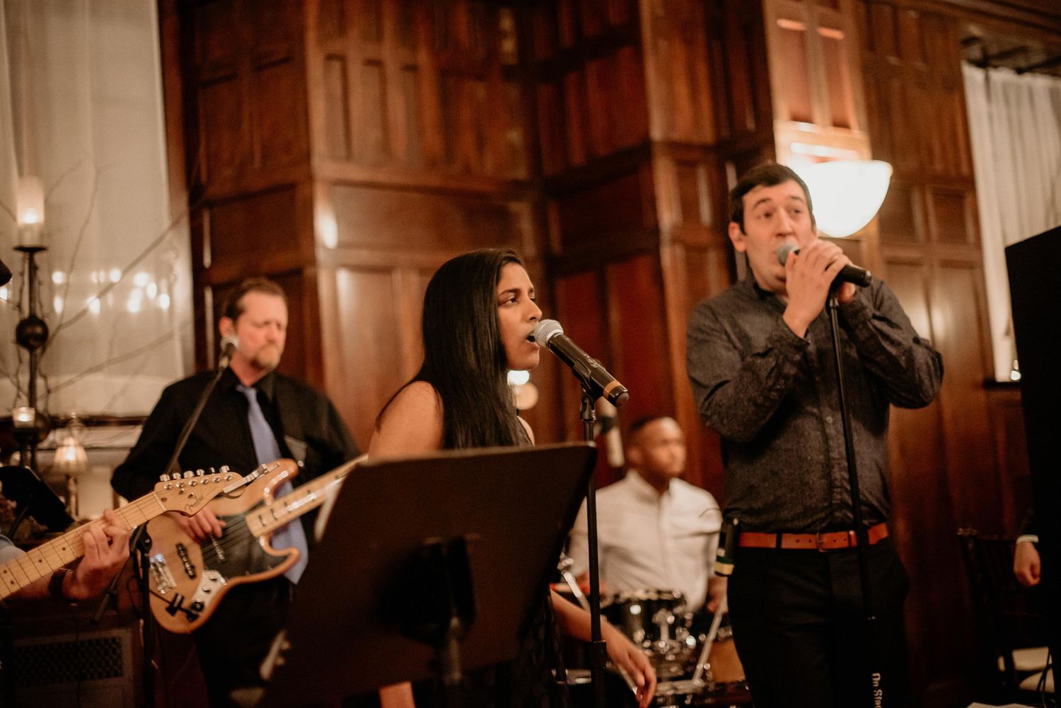 Live band performing at elegant venue with female vocalist singing into mic alongside male co-singer and guitarist.