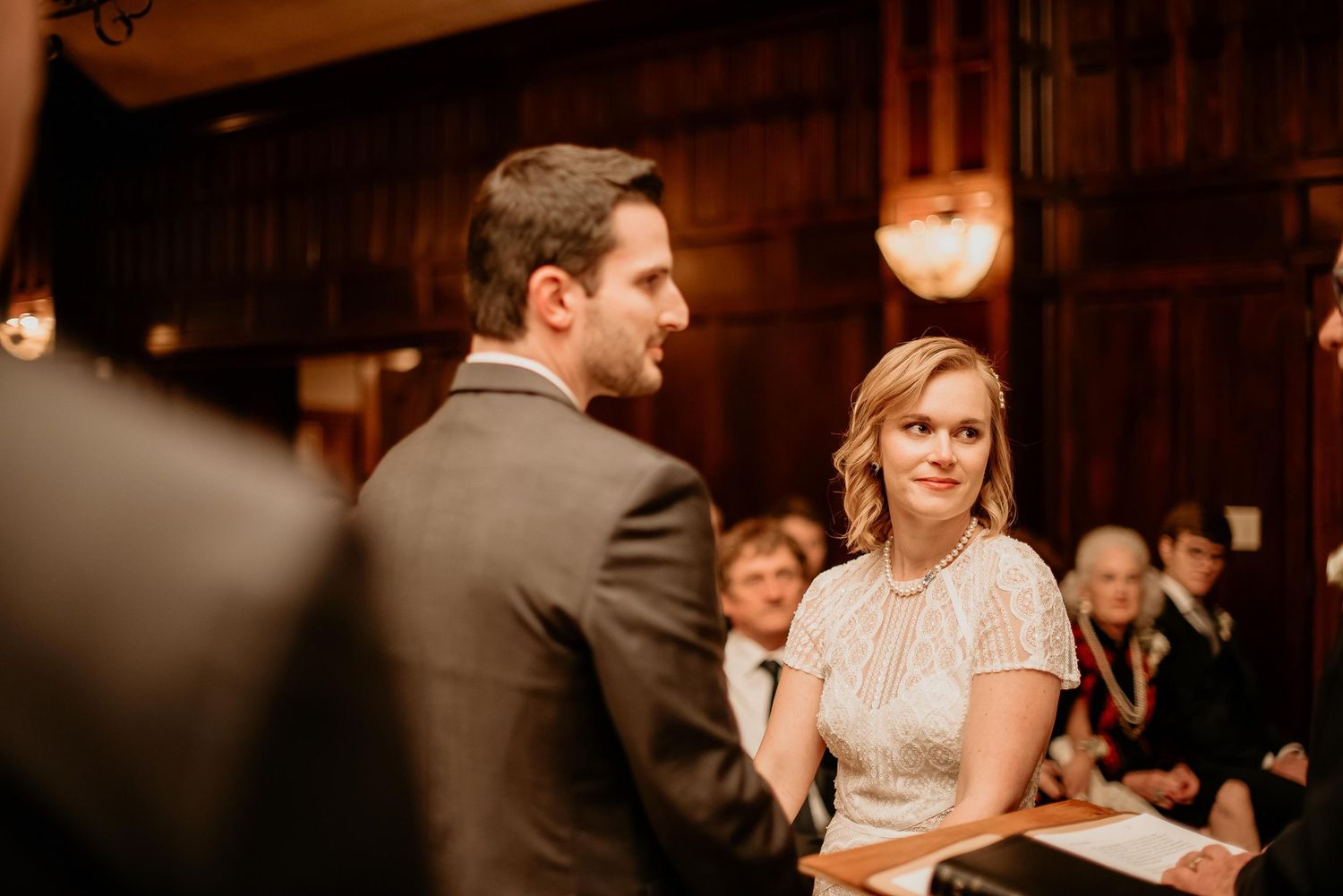 Bride and groom exchange vows in elegant wood-paneled venue during intimate wedding ceremony.