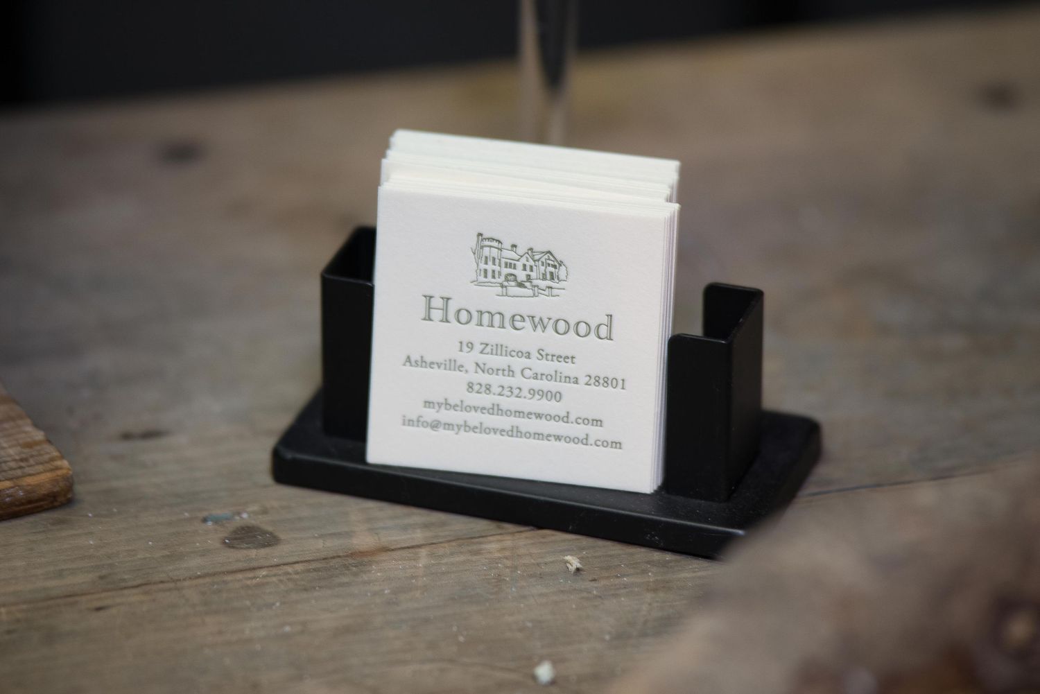 Black business card holder displaying Homewood Asheville North Carolina contact cards on a wooden surface.