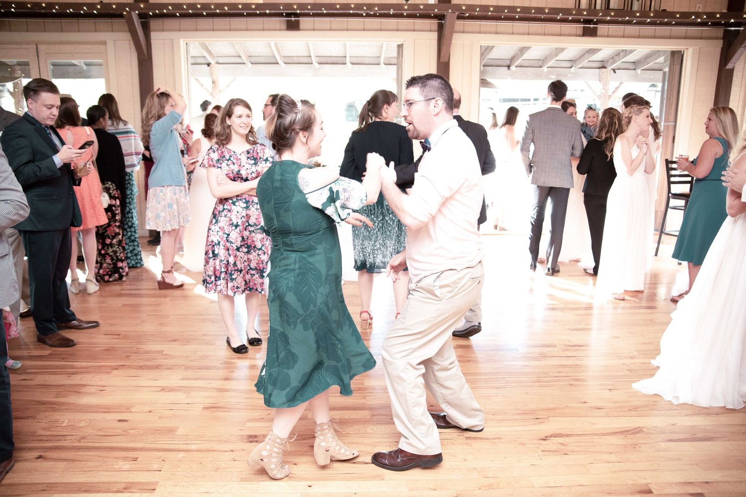 Guests dancing at a wedding reception on a wooden dance floor in a rustic venue.