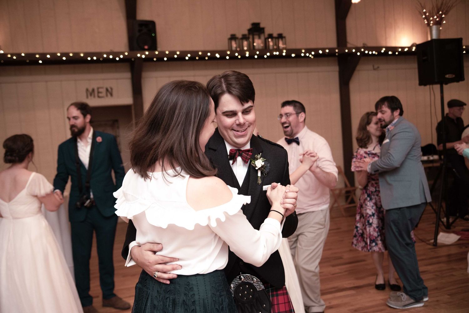 Groom in a tartan kilt shares a romantic slow dance with a guest at a wedding reception.