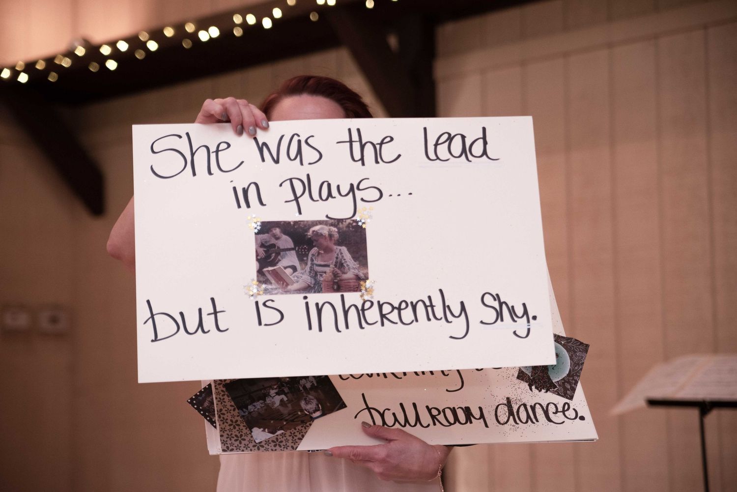 Person holding a handwritten sign reading she was the lead in plays but is inherently shy at a wedding reception.