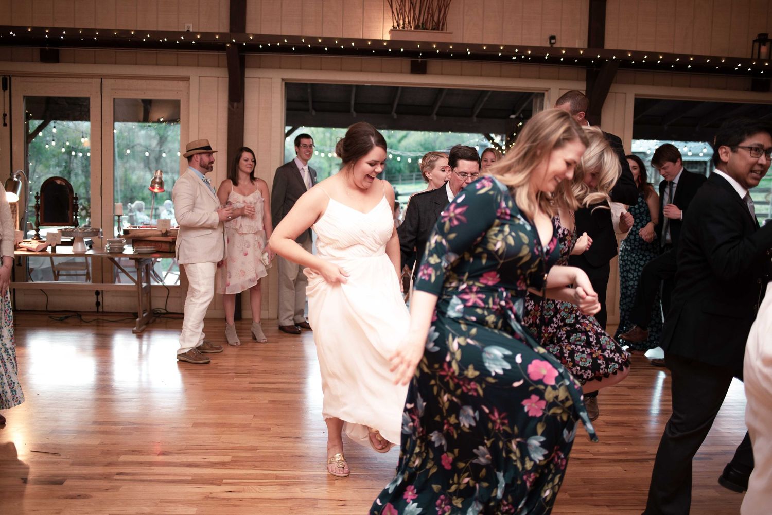 Wedding guests dancing energetically on wooden dance floor at rustic barn reception venue.