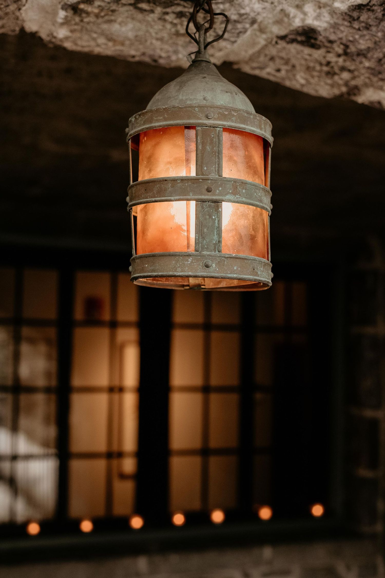 Vintage copper and iron hanging lantern glowing warmly against a dark stone ceiling with candles in background.