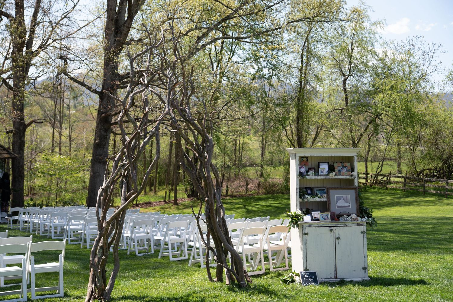 Outdoor wedding ceremony setup with white chairs on green grass surrounded by trees.
