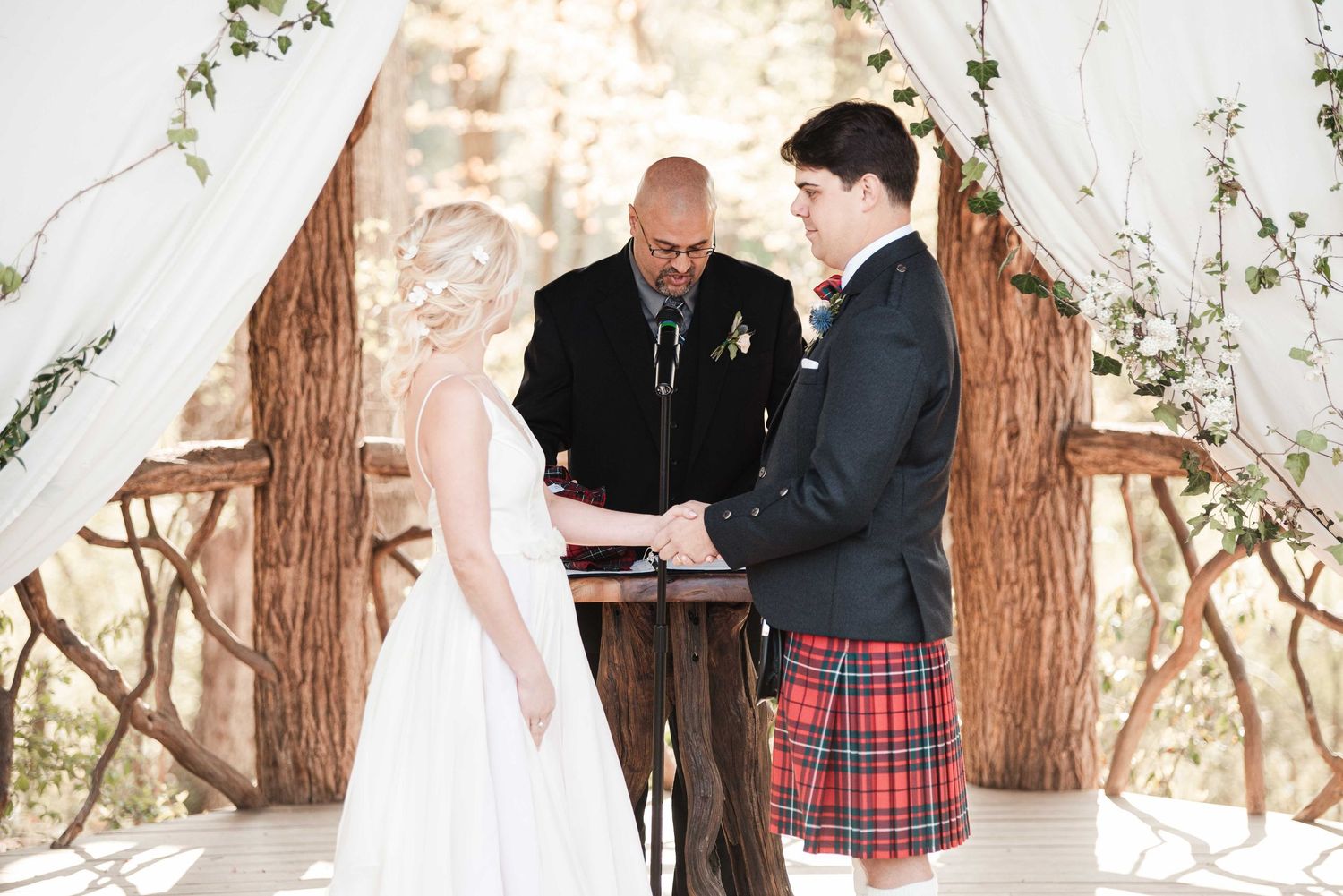 Bride and groom exchange vows at outdoor wedding ceremony, groom wearing traditional Scottish tartan kilt.