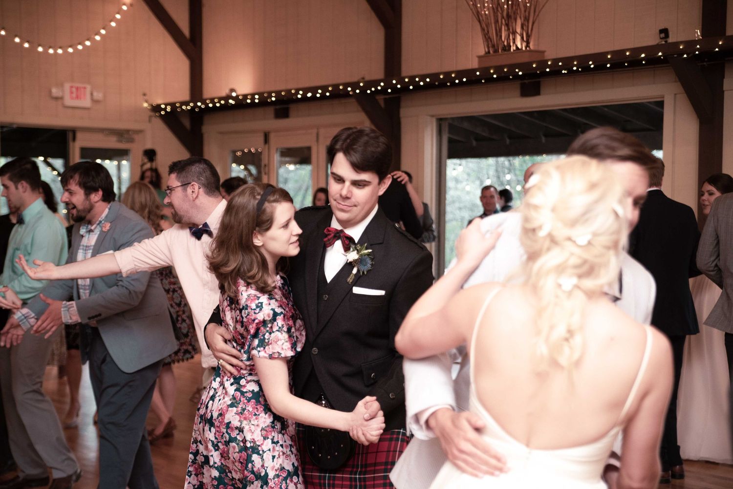 Guests dancing at a rustic wedding reception in a barn venue with string lights.