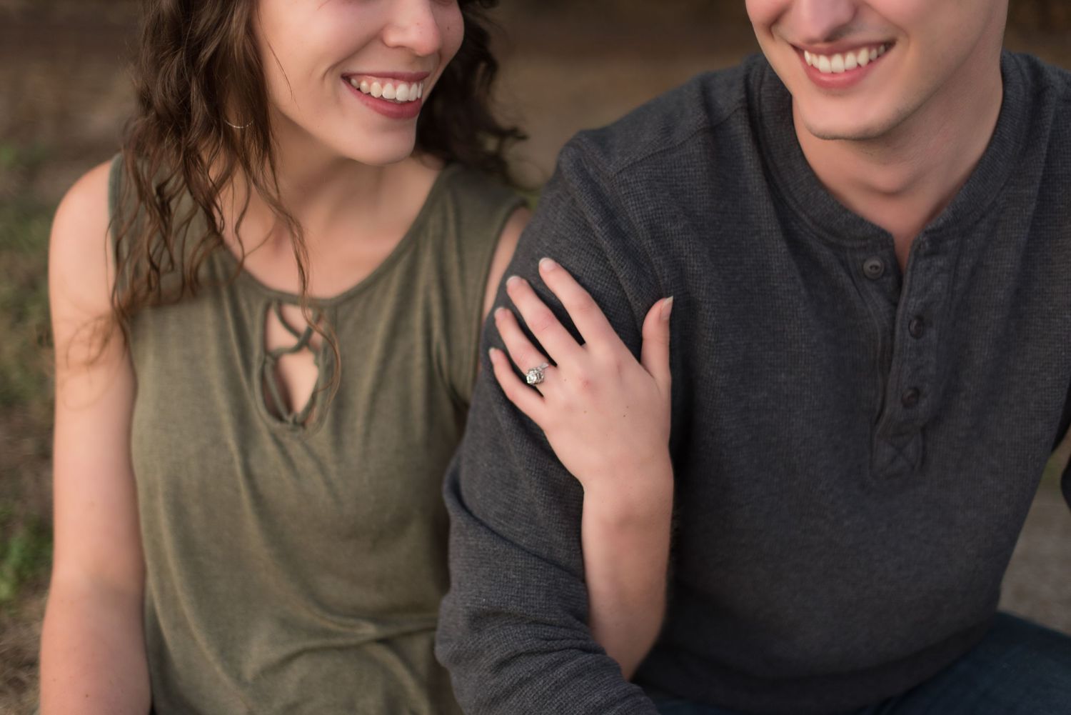 Smiling couple sitting closely together with engagement ring visible on womans hand.