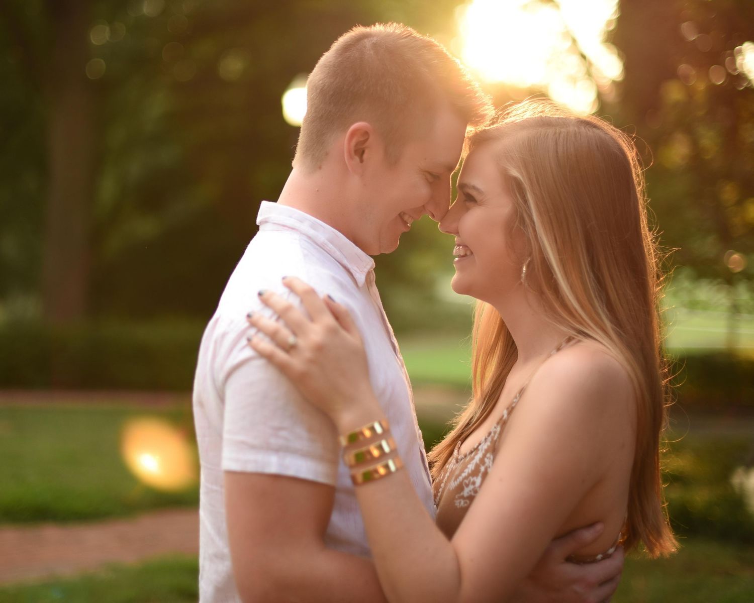 A couple shares a romantic moment at golden hour in a park, smiling and embracing.