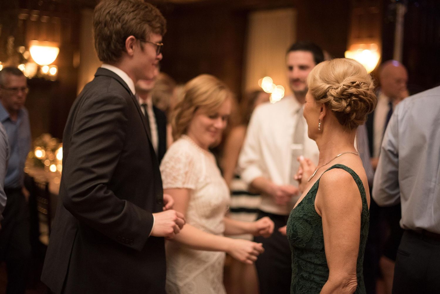 Elegant wedding reception guests dancing and socializing in a warmly lit ballroom, wearing formal attire.