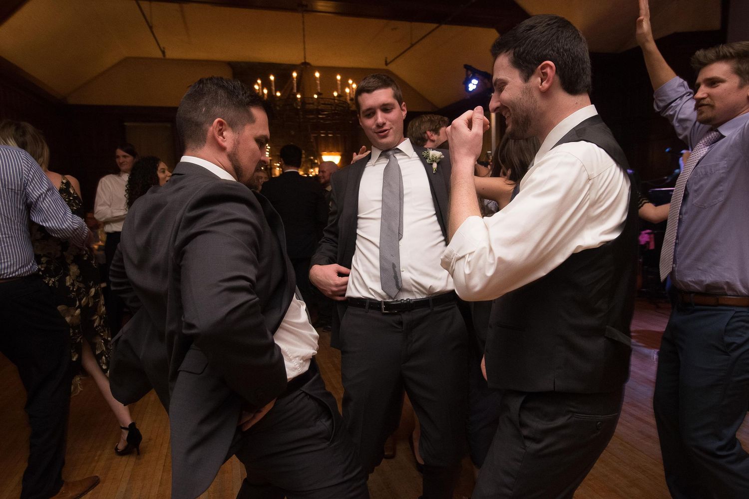 Men in suits dancing at a formal wedding reception in a dimly lit banquet hall.