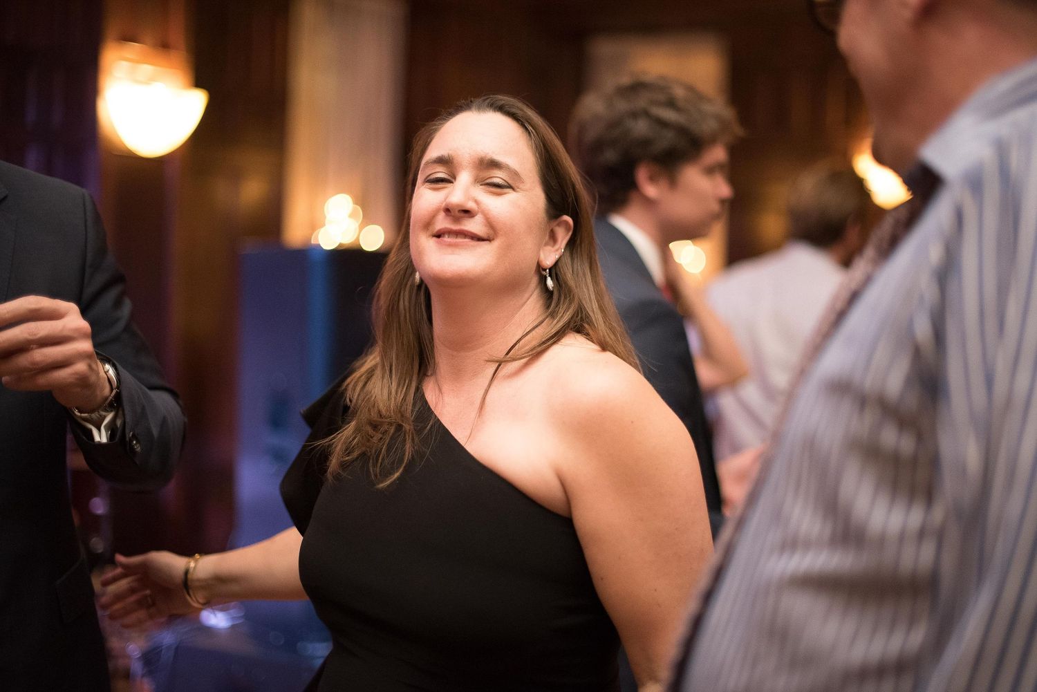 Woman in black dress smiling at elegant indoor social event.