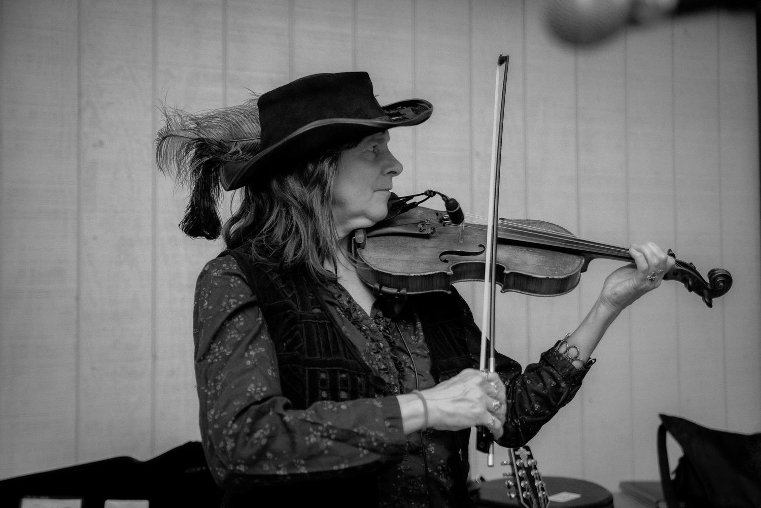 Black and white photo of a musician playing violin wearing a wide-brim hat with feathers.