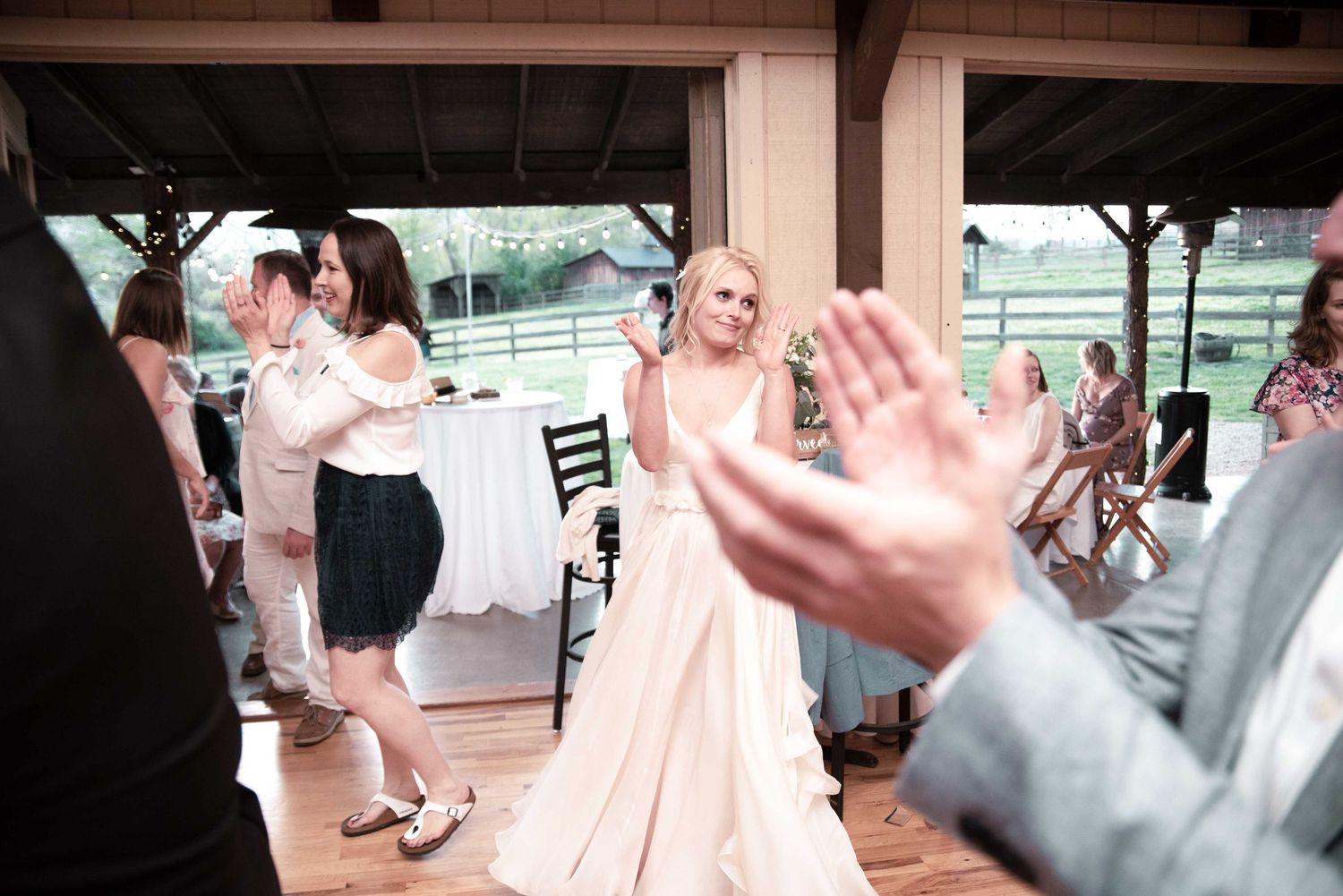 Bride in white gown dancing joyfully with guests at an outdoor wedding reception venue.