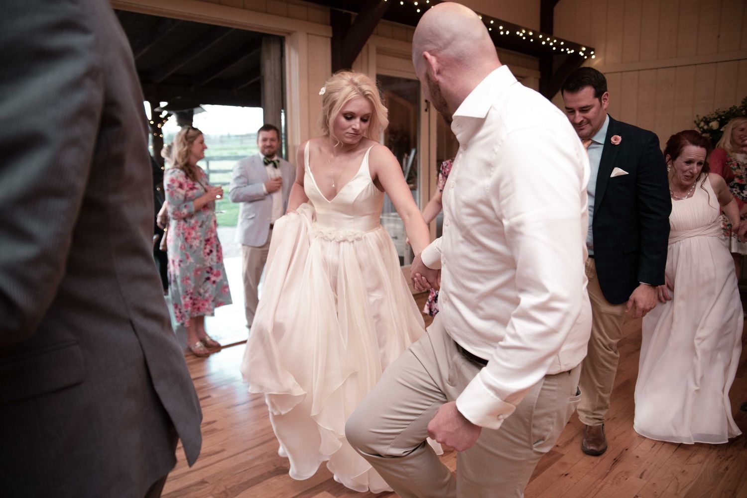 Bride in white gown dancing with groom at wedding reception while guests watch in rustic barn venue.