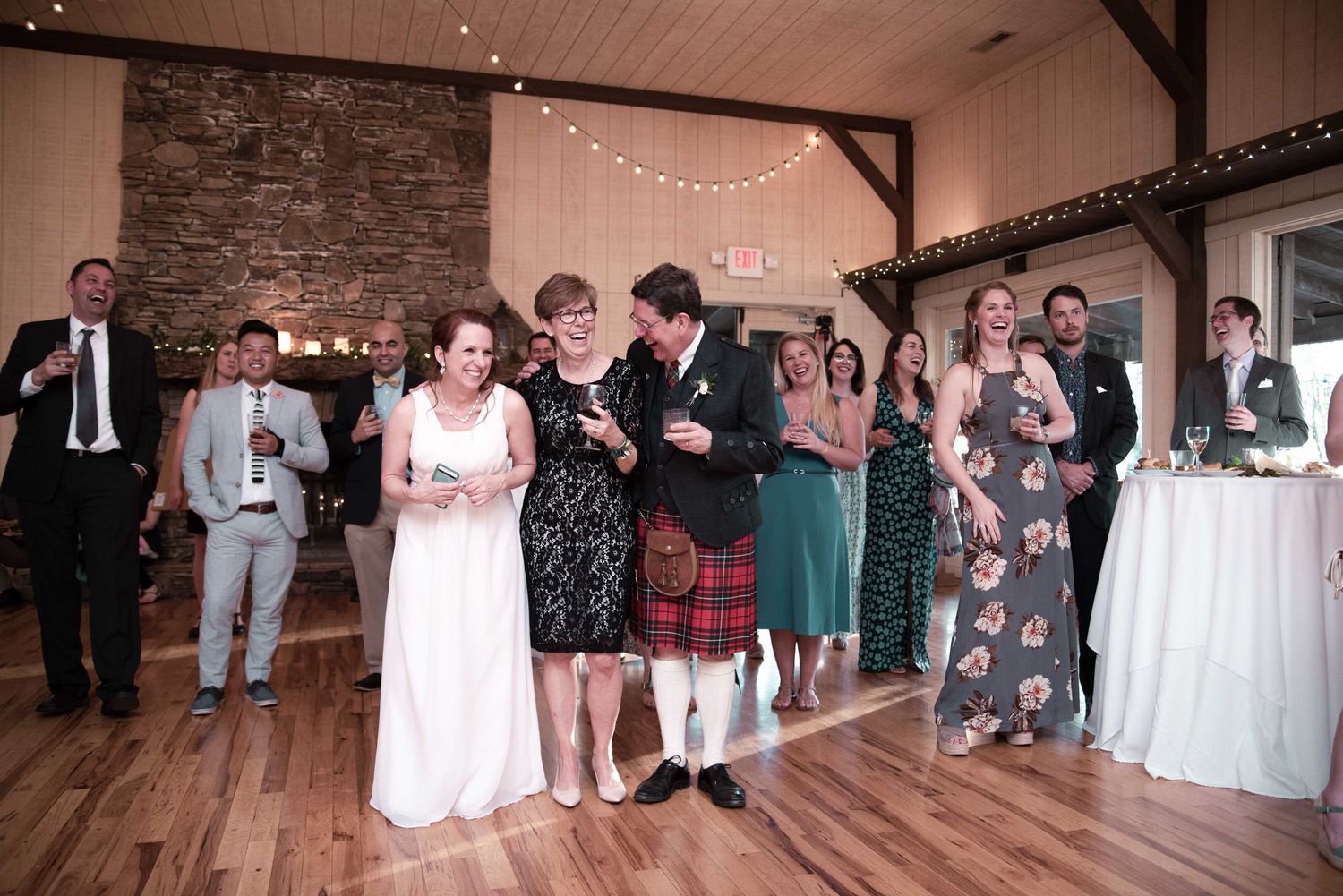Wedding reception guests celebrating on a wooden dance floor in a rustic barn venue with string lights.