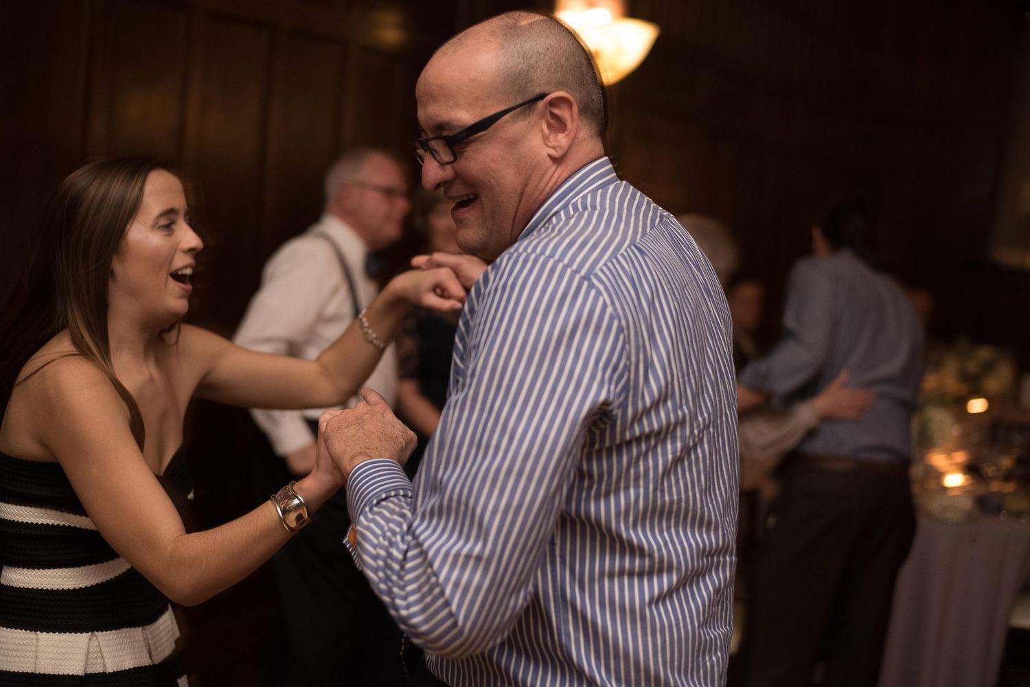 A couple laughs and dances together at an indoor evening reception event.