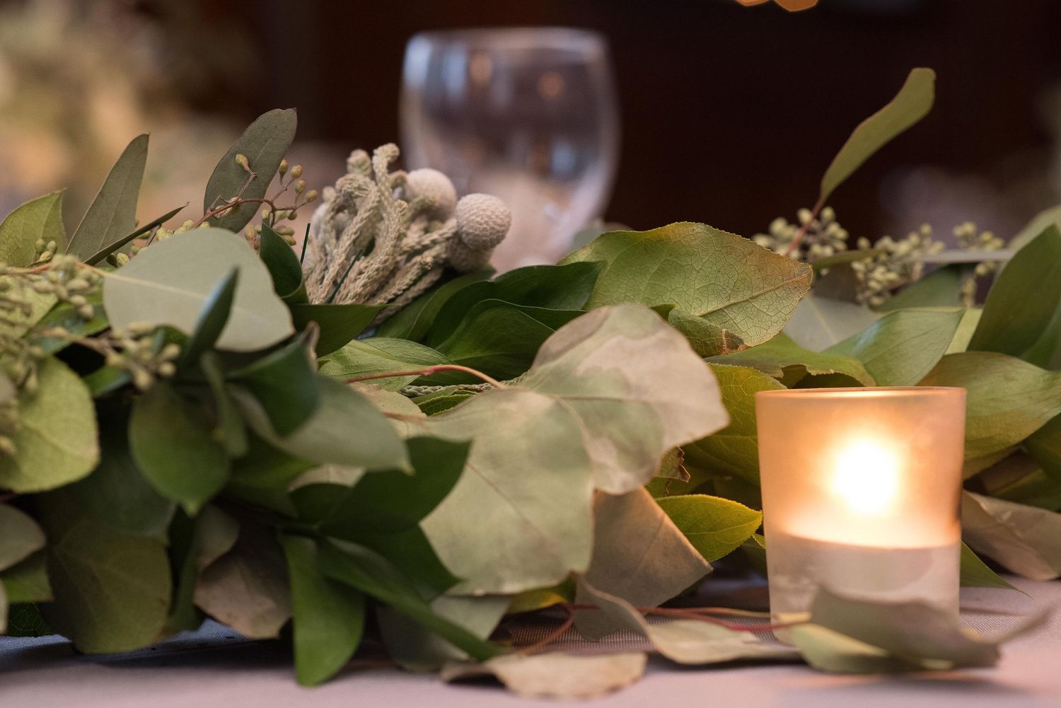 Elegant table centerpiece with green eucalyptus garland, silver berries, and a glowing votive candle.