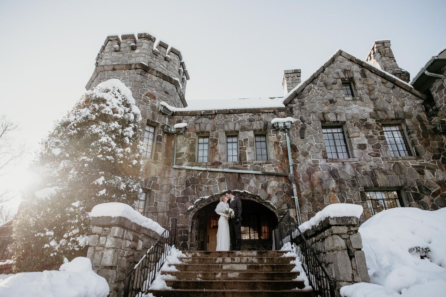 Bride and groom kissing on snowy castle steps in winter wedding photo.