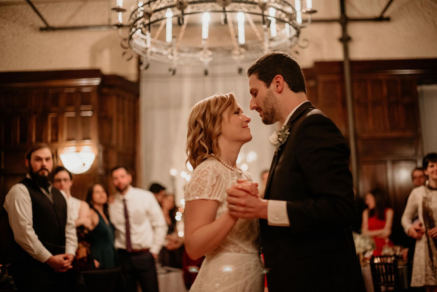 Bride and groom share their first dance under a chandelier at an elegant wedding reception.
