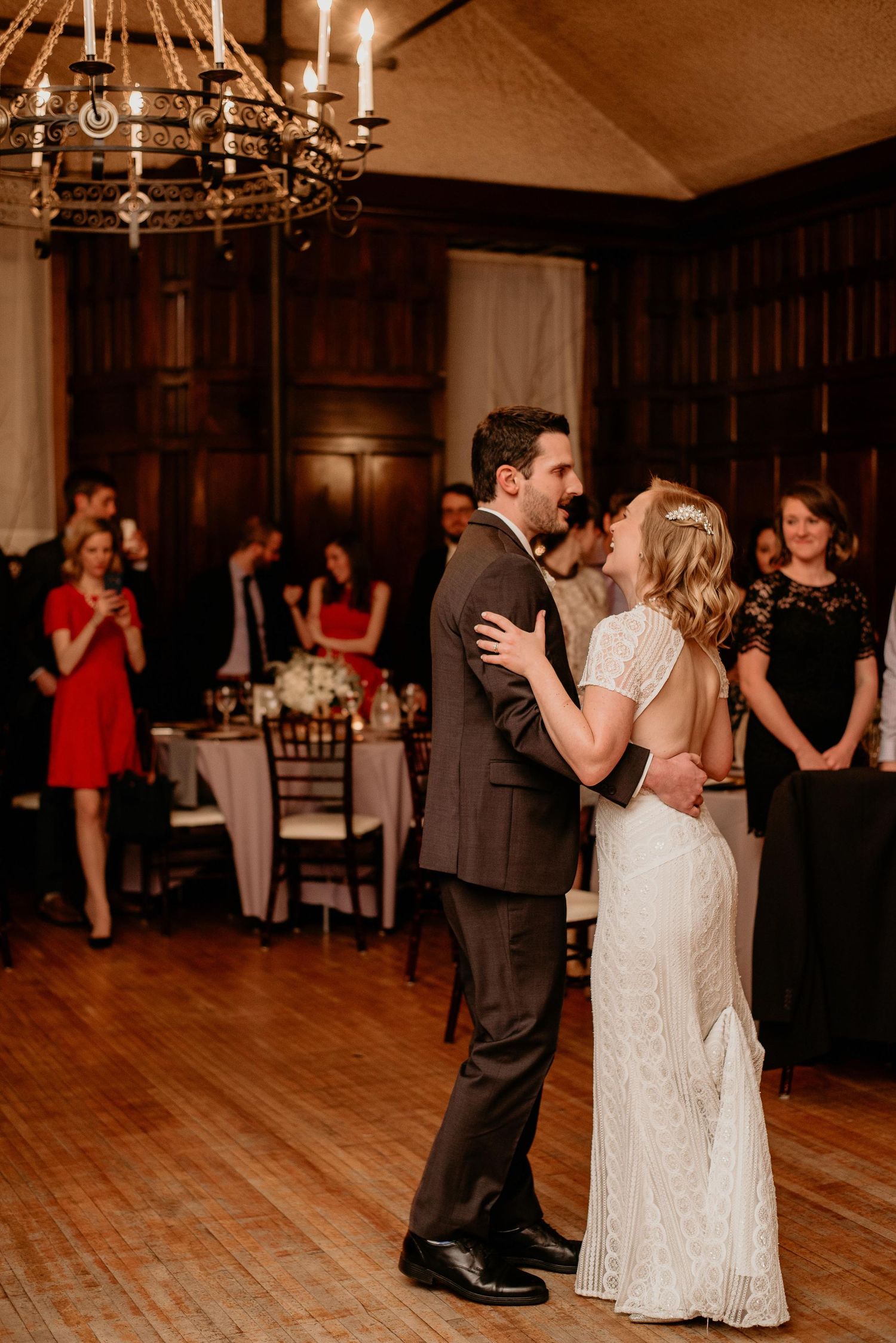 Bride and groom share their first dance in an elegant wood-paneled ballroom with chandelier lighting at their wedding reception.