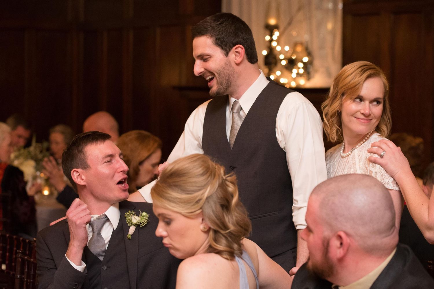 Wedding reception guests laughing and celebrating together in an elegant venue with warm string lights.