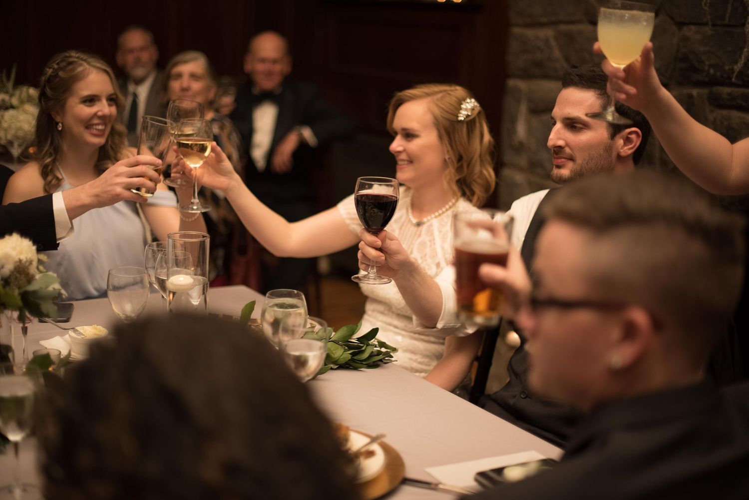Bride and bridesmaids raising glasses in a wedding toast at an elegant reception dinner.