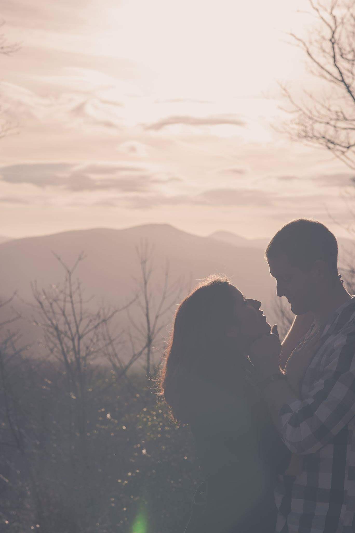 Romantic couple silhouette at sunset with mountain landscape and warm glowing sky.