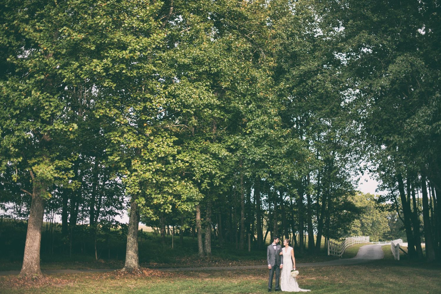 Bride and groom share a romantic moment surrounded by lush green trees in a scenic outdoor wedding setting.