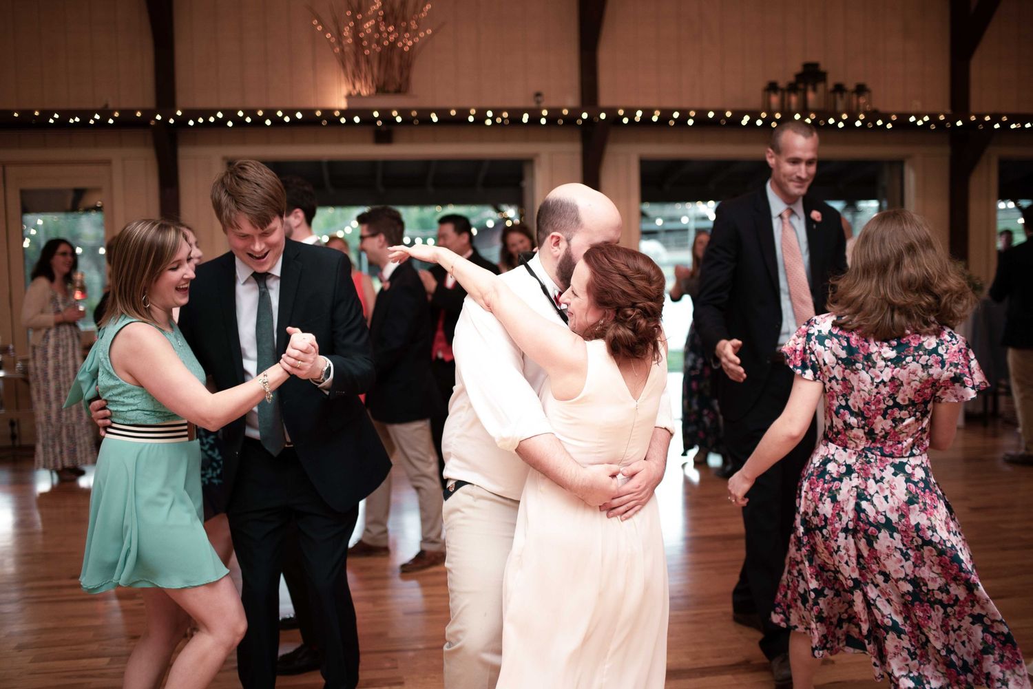 Guests dancing joyfully at a wedding reception in an elegantly decorated venue with warm string lights.