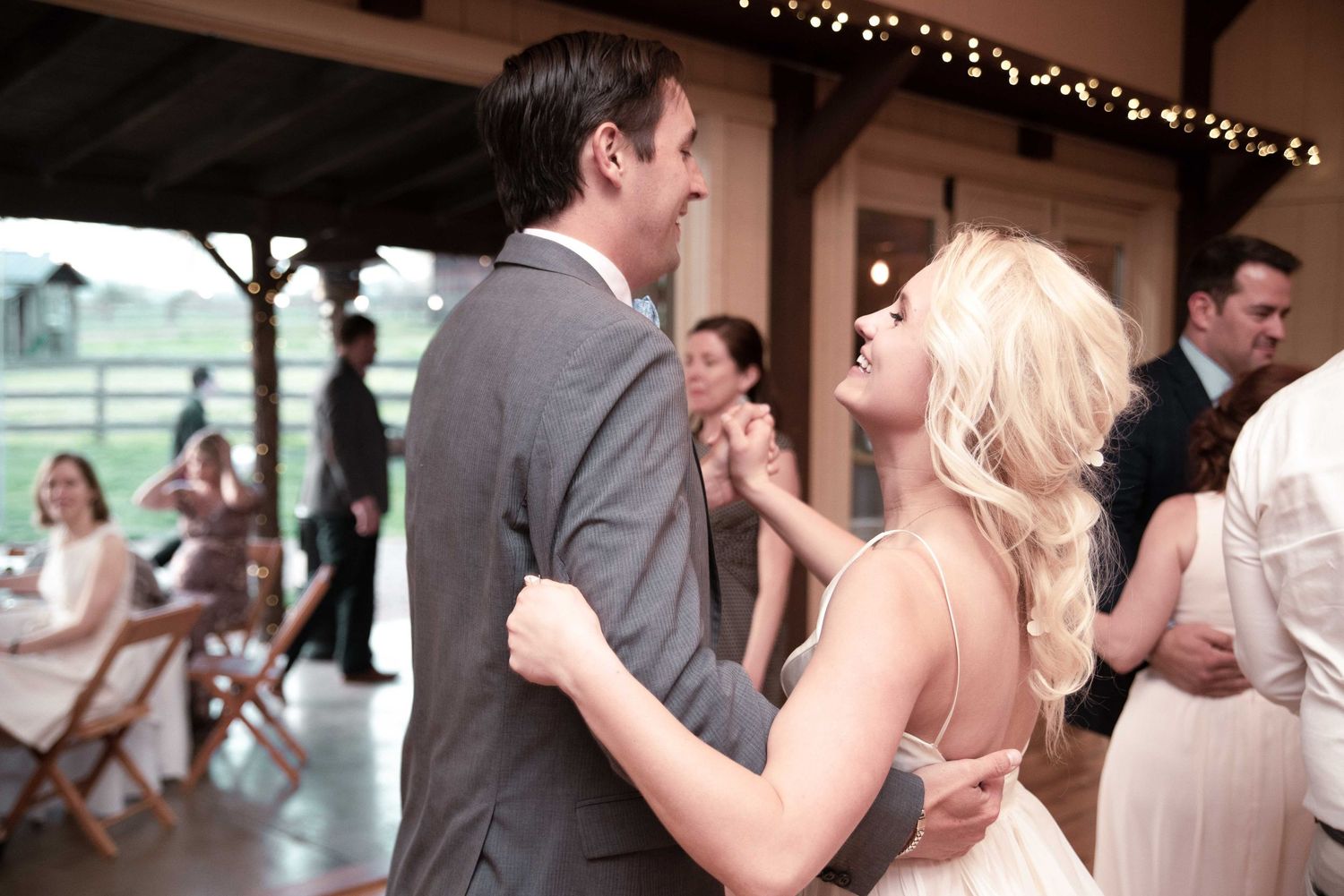 Couple shares romantic first dance at rustic wedding reception, bride laughing joyfully in backless gown.