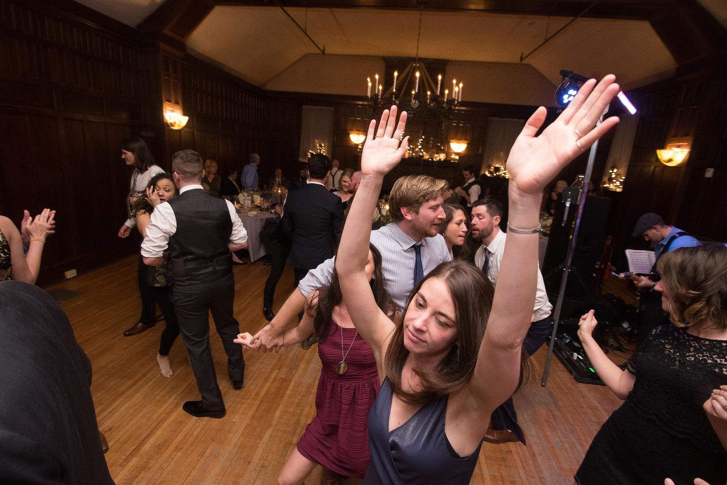 Guests dancing joyfully at an elegant wedding reception in a warmly lit ballroom with hardwood floors.