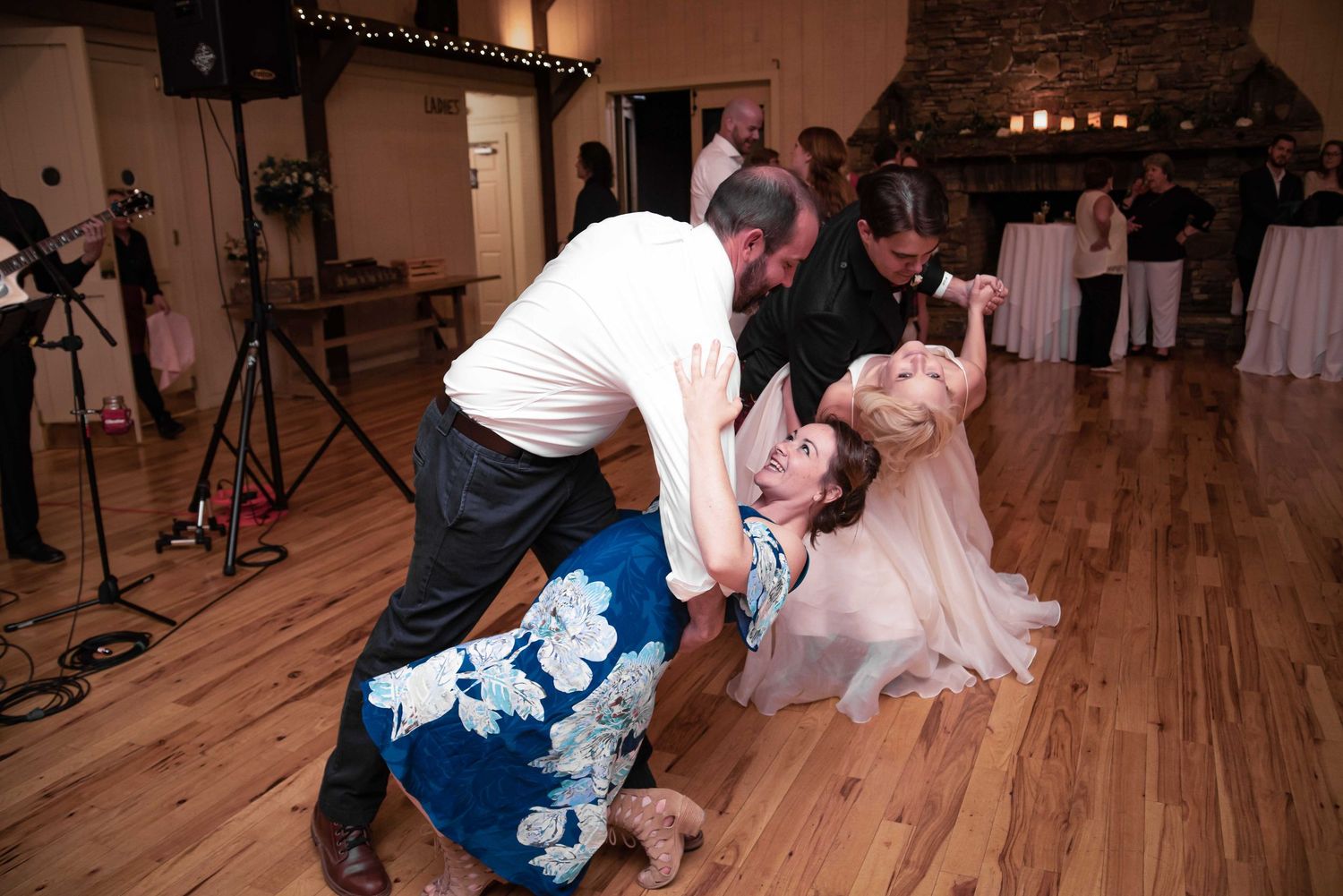 Guests dancing energetically on a wooden dance floor at a wedding reception in a rustic stone venue.