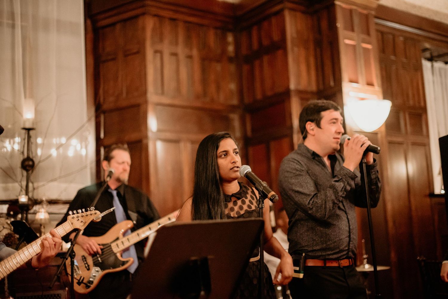 Live band performing at elegant venue with guitarist, female vocalist, and male singer with microphone.