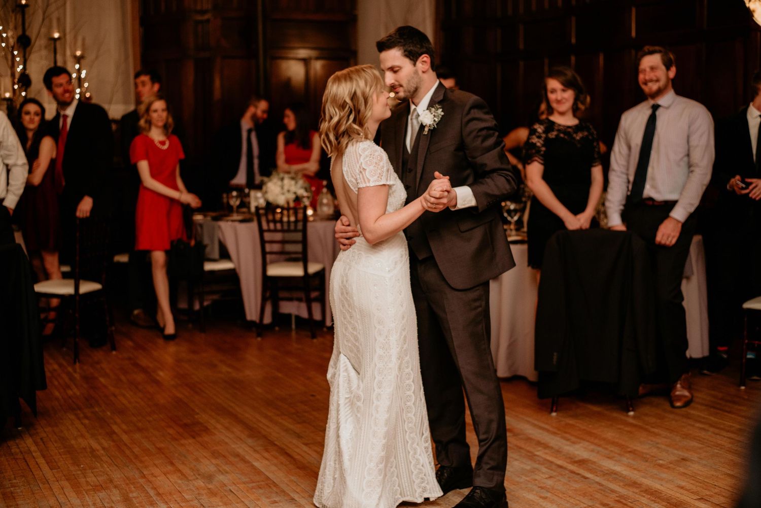 Bride and groom share their first dance at elegant wedding reception with guests watching in background.