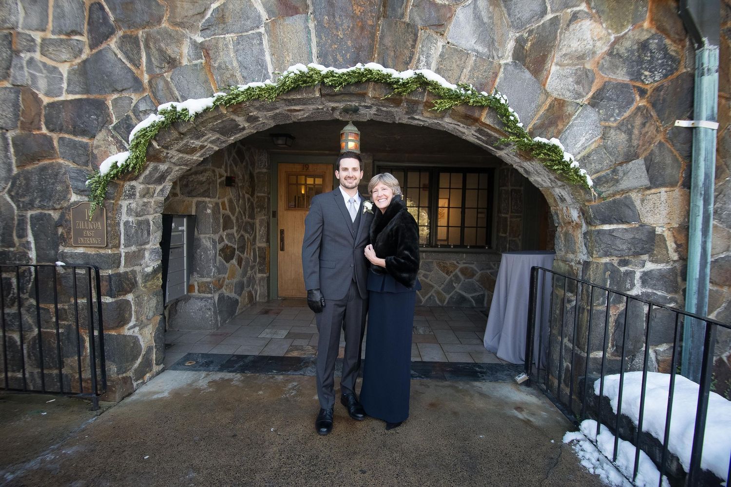 Couple posing under a stone arch entrance at a winter wedding venue with snow on the ground.