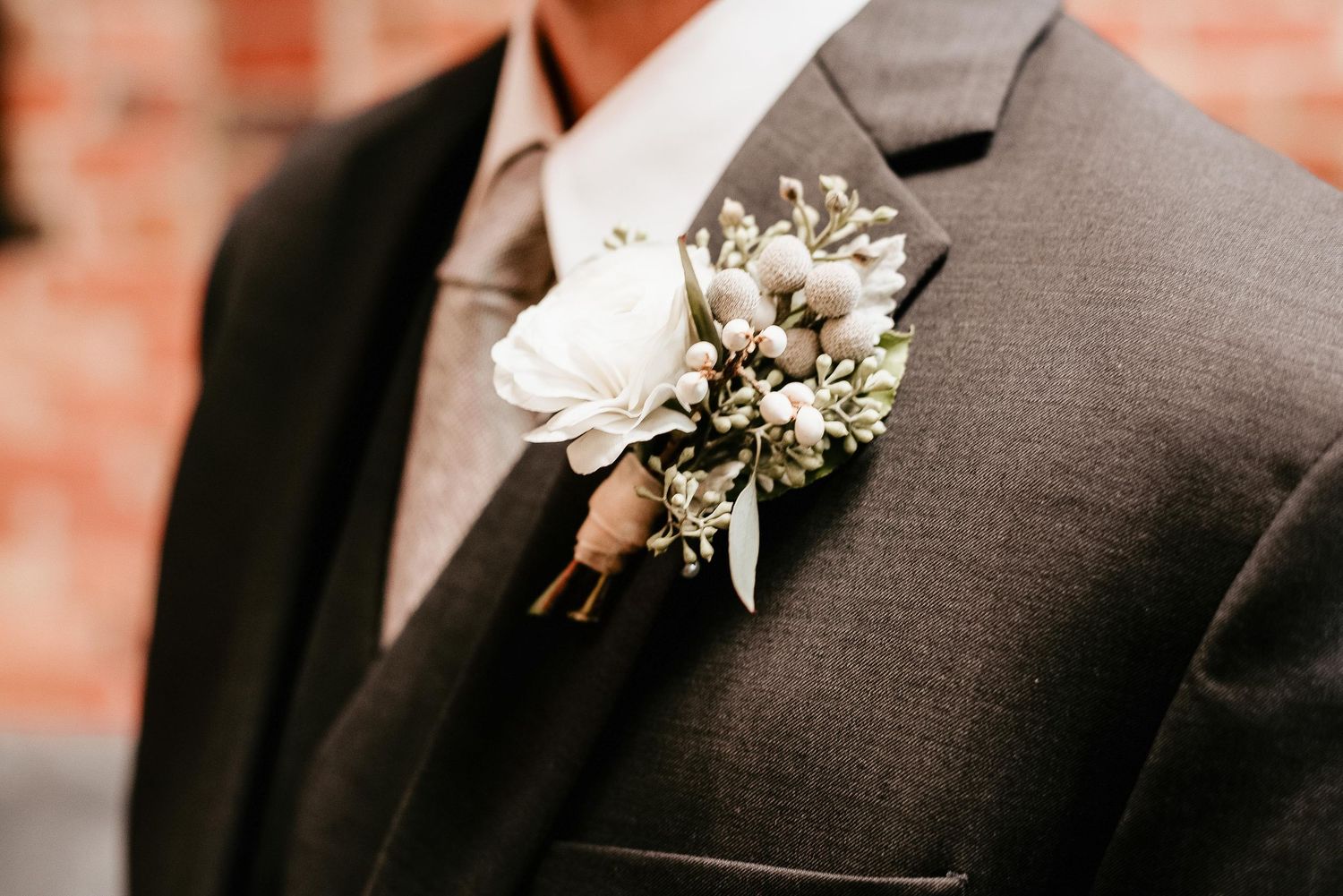 Close-up of a groom wearing a gray suit with an elegant white rose and baby's breath boutonniere on his lapel.